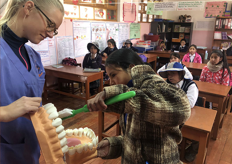 A volunteer shows a girl practices how to brush teeth correctly on oversized model